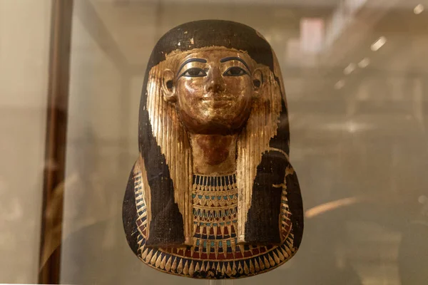 Kahire, Mısır; 21 Ocak 2024: Kahire, Mısır 'da bir müze cam kutusunda sergilenen Antik Mısırlı boyalı cenaze maskesi. Görüntü, detaylı işçiliği, korunmuş pigmentleri ve eğitim ve editörlüğe uygun tarihi gömme sanatını gösteriyor..