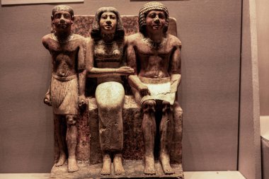 Kahire, Mısır; 21 Ocak 2024: Eski Krallık 'tan Antik Mısırlı aile heykeli, iki erkek figürle çevrili oturan bir kadın resmedildi. Boyalı kireçtaşına kazınmış bu cenaze heykeli soyu, sosyal kimliği ve ölümsüzlüğü simgeliyor..