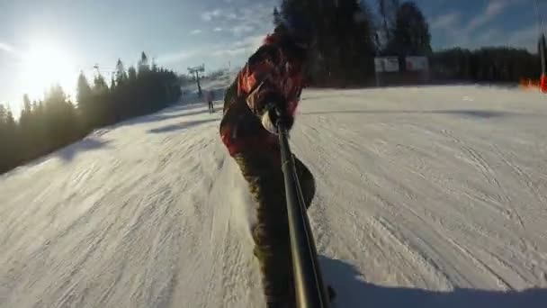 Hombre montando en snowboard con palo selfie en la mano — Vídeo de stock