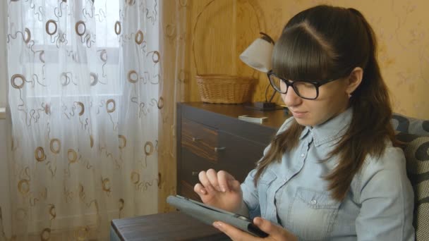 Mujer joven usando tableta electrónica sentada en un sofá — Vídeos de Stock