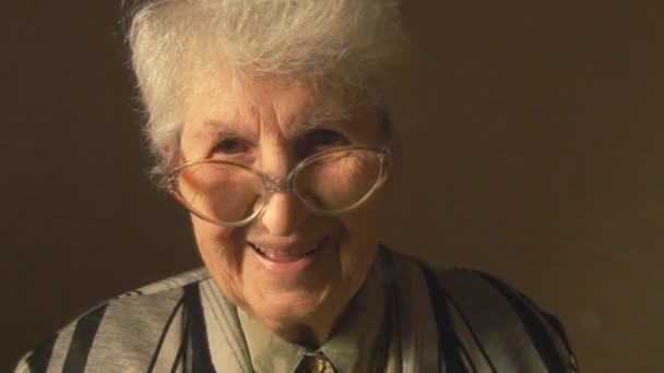 Old woman with eyeglasses looking at camera and smiling. — Stock Video