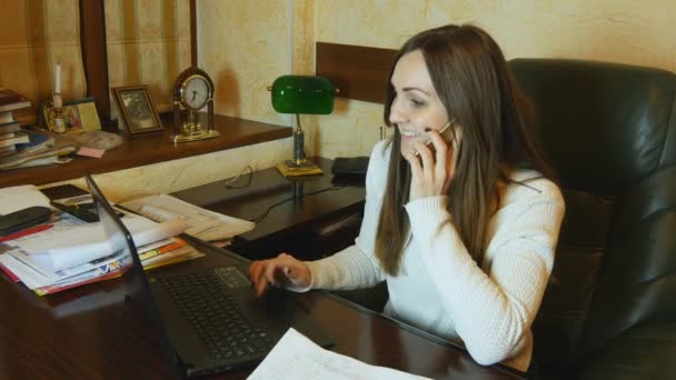 Hermosa mujer de negocios trabajando en el portátil y hablando por teléfono en la oficina — Vídeos de Stock