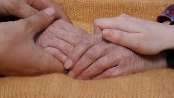 En ung mans och kvinnas händer tröstande ett par gamla händer av mormor utomhus — Stockvideo