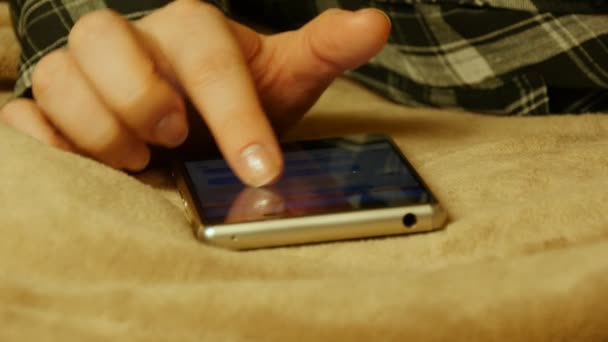Gros plan des mains féminines qui touchent le smartphone alors qu'elles sont allongées sur un drap de lit . — Video