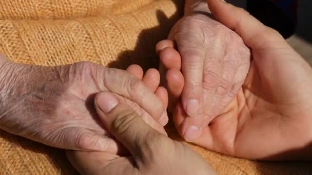 En ung manlig händer tröstande ett äldre par i händerna på mormor utomhus på nära håll. — Stockvideo