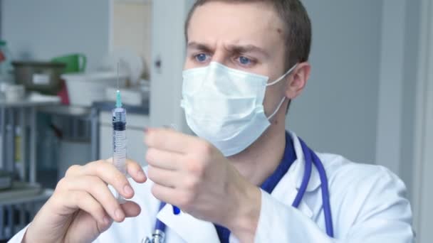 Retrato de um jovem médico caucasiano a deitar um líquido de uma seringa para um tubo, a olhar para o líquido azul num tubo de ensaio e a tirar a sua máscara protectora — Vídeo de Stock