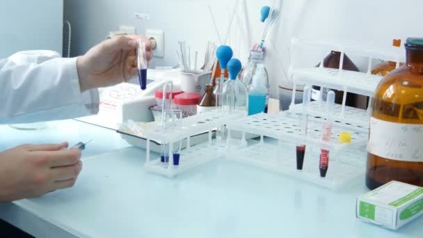 Doctor looking at blue liquid in a test tube and put on the cap from a syringe — Stock Video