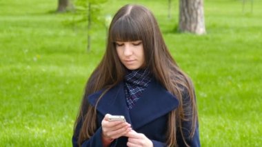 Güzel kadın hücre smartphone açık havada park - ayrıntı kullanır. Genç çekici mutlu kız bir şehir parkında rahatlatır ve bir cep telefonu kullanır. O çok mutlu ve memnun görünüyor