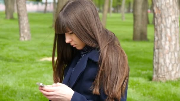 Hermosa mujer esperando encontrarse en el parque - detalle. Ella mirando a su alrededor y utiliza el teléfono inteligente mibile . — Vídeos de Stock