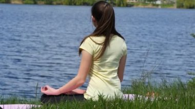 Genç kadın Sahilde meditasyon rahatlatıcı. Çimenlerin üzerinde oturan kız ve lotus pozisyonu sırasında yoga egzersizleri yapıyor nehir yanında meditasyon