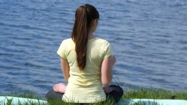 Meditasyon ve lotus pozisyonu kulaklık müzik dinleme genç kadın. Çimenlerin üzerinde oturan ve nehrin yanında Sahilde meditasyon rahatlatıcı kız