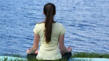 Genç kadın Sahilde meditasyon rahatlatıcı. Çimenlerin üzerinde oturan kız ve lotus pozisyonu sırasında yoga egzersizleri yapıyor nehir yanında meditasyon