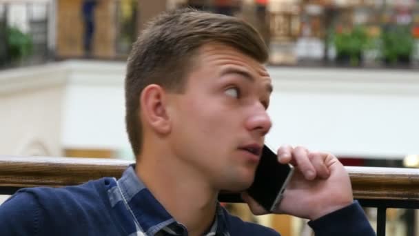 Joven hombre guapo hablando en el teléfono celular en el centro comercial y sonriendo — Vídeo de stock