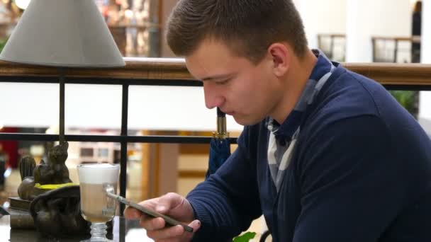 Alışveriş Merkezi kafede Smartphone kullanan genç yakışıklı adam. Yakın çekim adam bilgi tarama ve akıllı telefon resimleri kaydırma — Stok video
