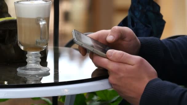 Manliga händer användande smartphone och har cappuccino Café i köpcentrum. Närbild av man surfar information och rullning bilder på smart telefon — Stockvideo