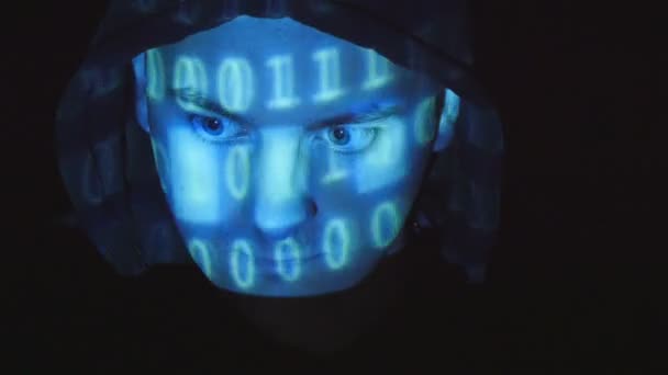 Hooded hacker working on a computer, binary code projecting on his face. Source code projected over an angry hostile mans face, black background. — Stock Video