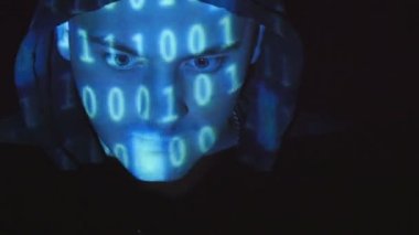 İkili kod yüzünde projelendirme bir bilgisayarda çalışan kukuletalı hacker. Yüzünde siyah arka plan kızgın bir düşman öngörülen kaynak kodu mans.