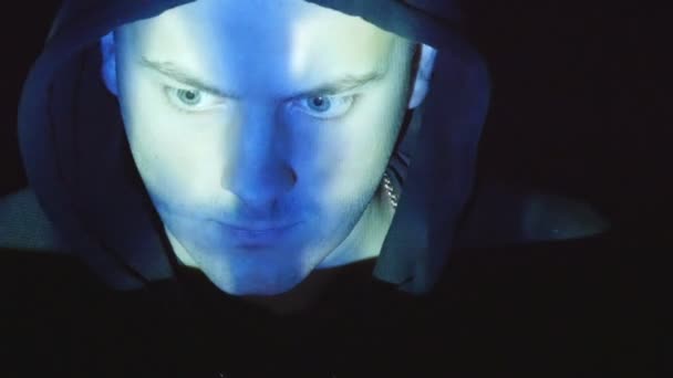 Hooded hacker working on a computer, binary code projecting on his face. Source code projected over an angry hostile mans face, black background — Stock Video