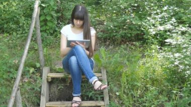 Ahşap merdiven ormanın içinde oturan ve tablet PC'yi kullanma güzel ve genç birbayan. Internet tarama, app kullanarak ve açık havada iletişim mutlu kız. Sakin ol ve teknoloji.