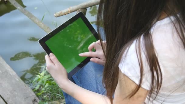 Kvinnliga händer med digital TabletPC med grön skärm sitter på en trä brygga vid sjön. — Stockvideo