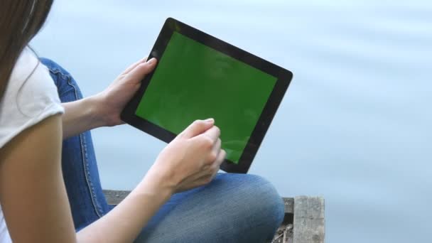 Mladá dívka pomocí digitálních tablet pc s zelenou obrazovkou na dřevěné molo u jezera. Zadní pohled..