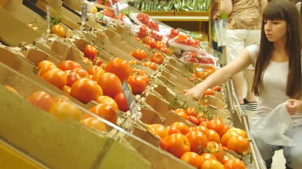 Genç güzel kız bir bakkal süpermarket domates seçmek ve konuşuyor. Çekici kadın markette taze olgun kırmızı domates seçilmesi üretmek bölümü. — Stok video