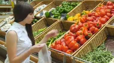 Genç güzel kız biber bir bakkal süpermarket seçmektir. Çekici kadın markette taze olgun kırmızı biber seçme üretmek bölümü.