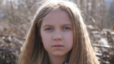Küçük üzgün bir çocuğun portresi baharın başında bulanık bir ormanın arka planına karşı. Dışarıdaki kameraya bakan ciddi bir kız. Yüzünde mutsuz ifade olan kadın çocuğun duygularını kapat..