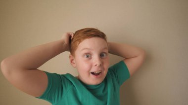 Çilli, mutlu, kızıl saçlı çocuk kameraya bakıyor ve el kaldırıyor. İçindeki başarıyı alkışlıyor. Kapalı mekanda yüzünde olumlu duygular olan kızıl saçlı bir çocuğun portresi. Yavaş çekim.