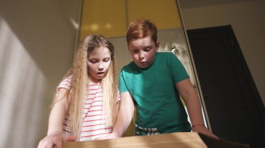 Mutlu küçük kız ve erkek kardeş karton kutuyu açıp odadayken ondan hediye alıyorlar. Şaşırmış küçük kız ve oğlan yüzlerinde neşe ve şaşkınlık ifadesi var. Şirin çocuklar sunmaktan zevk alıyor..