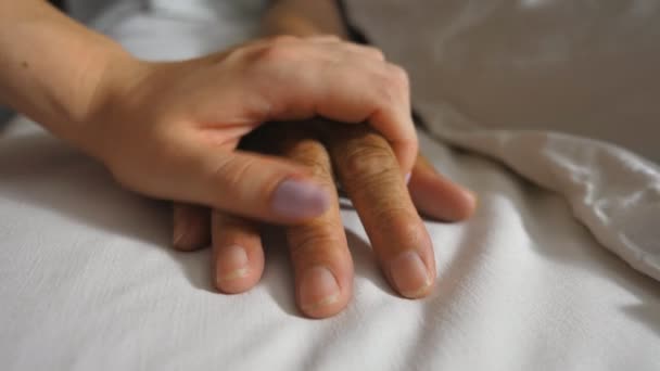 La nipote conforta il braccio rugoso della nonna matura malata che giace nell'ospedale a letto. Ragazza delicatamente tocca la mano di sua nonna in clinica medica. Figlia mostra cura e amore per sua madre — Video Stock