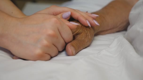 Enkelin hält und tröstet Hand ihrer Großmutter in Klinik Die Tochter berührt sanft den faltigen Arm der kranken, reifen Mutter, die im Krankenhaus liegt. Konzept von Fürsorge und Liebe. Zeitlupe — Stockvideo