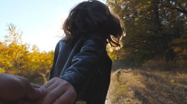 Beni takip edin. Mutlu kız, erkek arkadaşını sonbahar ormanının yakınına götürüyor. Genç bir kadın erkeğin elini tutuyor ve ormanlık alanda yol boyunca koşuyor. Arka planda güzel bir doğa. Sevgi kavramı. POV