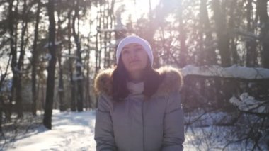 Kışın giyinmiş, bir avuç kar fırlatan ve düşen kar tanelerinin tadını çıkaran genç ve mutlu bir kadın. Güzel bir kış gününde karla oynayan çekici bir kız. Kış tatili kavramı. Ağır çekim. Yaklaş.