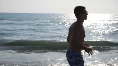 Atletik yakışıklı adam sabah deniz kıyısında koşuyor. Okyanus sahilinde koşan genç sporcu. Deniz kıyısında spor yapan erkek sporcuya yaklaş. Sağlıklı aktif yaşam tarzı. Ağır çekim kenar görünümü