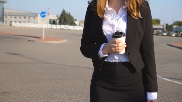 Młoda bizneswoman z filiżanką kawy spaceruje w pobliżu parkingu w słoneczny dzień. Kobiece nogi w butach na wysokich obcasach w miejskiej ulicy. Bizneswoman idzie do pracy. Powolny ruch Zamknij — Wideo stockowe