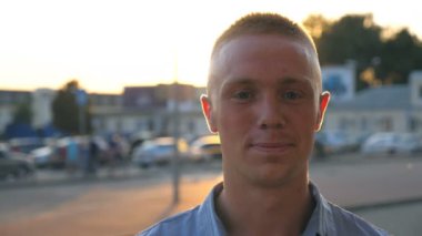 Gün batımında şehir sokağındaki kameraya bakıp gülümseyen genç ve mutlu iş adamlarına yakın durun. Arka planda güneş ışığı olan şehir ortamında duran gömlekli başarılı bir adamın portresi.