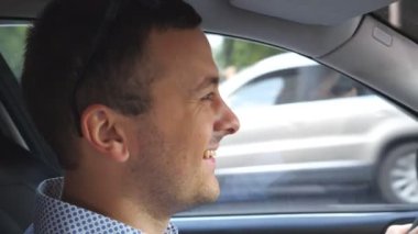 Şehir merkezinde tişörtlü, gülümseyen ve otomobil kullanan mutlu genç bir iş adamı. Şehirde araba süren bir erkek sürücü. İşe gidip gelen yakışıklı bir adam. Kuaförden yan görüntü. Yavaşça kapat.