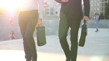 Evrak çantalı iki işadamı arka planda güneş ışığıyla şehir caddesinde yürüyor. İş adamları işe birlikte gider. Kendine güvenen adamlar ofise doğru geliyor. Meslektaşlar dışarı çıkıyor. Yavaş çekim