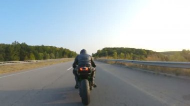 Güneşli bir sonbahar gününde otoyolda motosiklet süren motosikletliyi takip edin. Motosikletli, kır yolunda motosikletiyle yarışıyor. Yolculuk sırasında bisiklet süren bir adam. Yolculuk kavramı. Hava görüntüsü