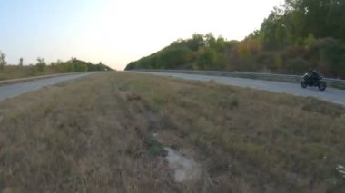 Anayolda motosiklet süren motosikletliyi takip edin. Motosikletli, kır yolunda motosikletiyle yarışıyor. Yolculuk sırasında bisiklet süren adam. Yolculukta özgürlük ve macera kavramı. Hava görüntüsü