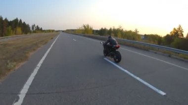 Günbatımında şehir yolunda motosikletle gezen motosikletliyi takip edin. Motosikletli otoyolda motosikletiyle yarışıyor. Yolculuk sırasında bisiklet süren adam. Yolculuk ve özgürlük kavramı. Hava görüntüsü
