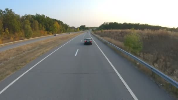 田舎道で黒い車の運転の空中ビュー。旅行中に高速道路に沿って自動車に乗る。高速道路に沿って移動する自動車を飛び越える。旅行での自由と冒険の概念。バックビュー — ストック動画