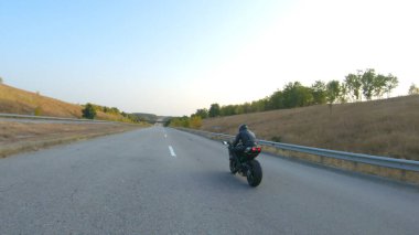 Anayolda motosiklet süren motosikletliyi takip edin. Motosikletli, kır yolunda motosikletiyle yarışıyor. Yolculuk sırasında bisiklet süren adam. Yolculukta özgürlük ve macera kavramı. Hava görüntüsü.