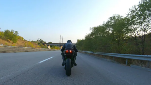 Anayolda motosiklet süren motosikletliyi takip edin. Motosikletli, kır yolunda motosikletiyle yarışıyor. Yolculuk sırasında bisiklet süren adam. Yolculukta özgürlük ve macera kavramı. Kapat..