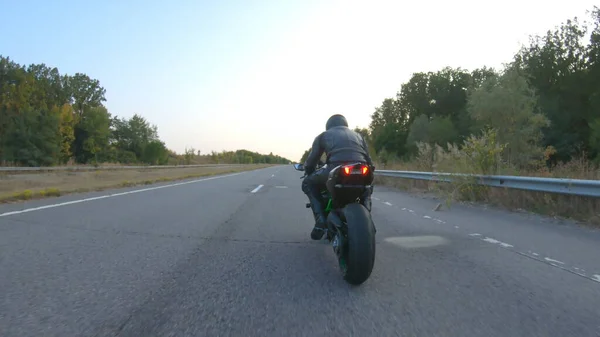 高速道路で現代のスポーツバイクに乗ってバイカーの周りを移動するカメラ オートバイ愛好家は日没時に田舎道でバイクレースをする 旅行中に自転車を運転する男 自由と冒険の概念 — ストック写真