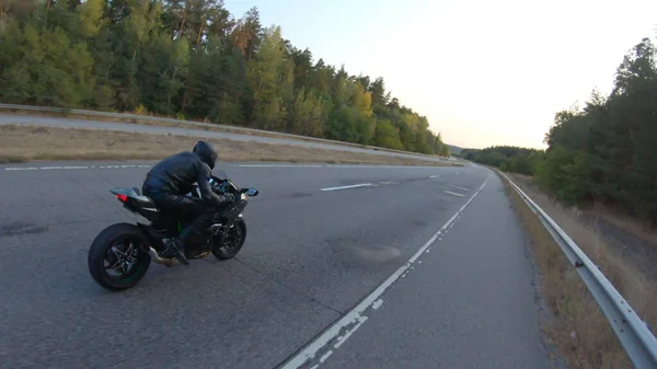 Camera moving around of biker riding on modern sport motorbike at highway. Motorcyclist racing his motorcycle on country road at sunset. Man driving bike during trip. Concept of freedom and adventure.