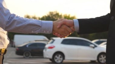 Arka planda arabalarla el sıkışan iki işadamı. Menajer, satıcı ve müşteri arasında tokalaşma. Erkek kollarını dışarıda sallıyor. Yavaşça kapat.