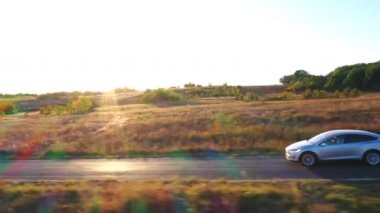 Kırsal yolda hızla giden elektrikli arabanın hava manzarası. Arka planda güzel güneşli bir manzara. Modern araç otoyolda hızla ilerliyor. Ekoloji dostu otomobil elektrik yüküne biniyor