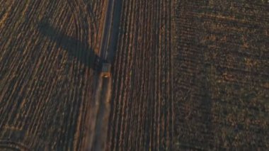 Tarlalar arasında boş kırsal yolda giden çiftçi cipinin hava görüntüsü. Alacakaranlıkta tozlu yolda hız yapan off-road aracı. Yaz günü kırsal kesimde araba sürerken. Üst görünüm